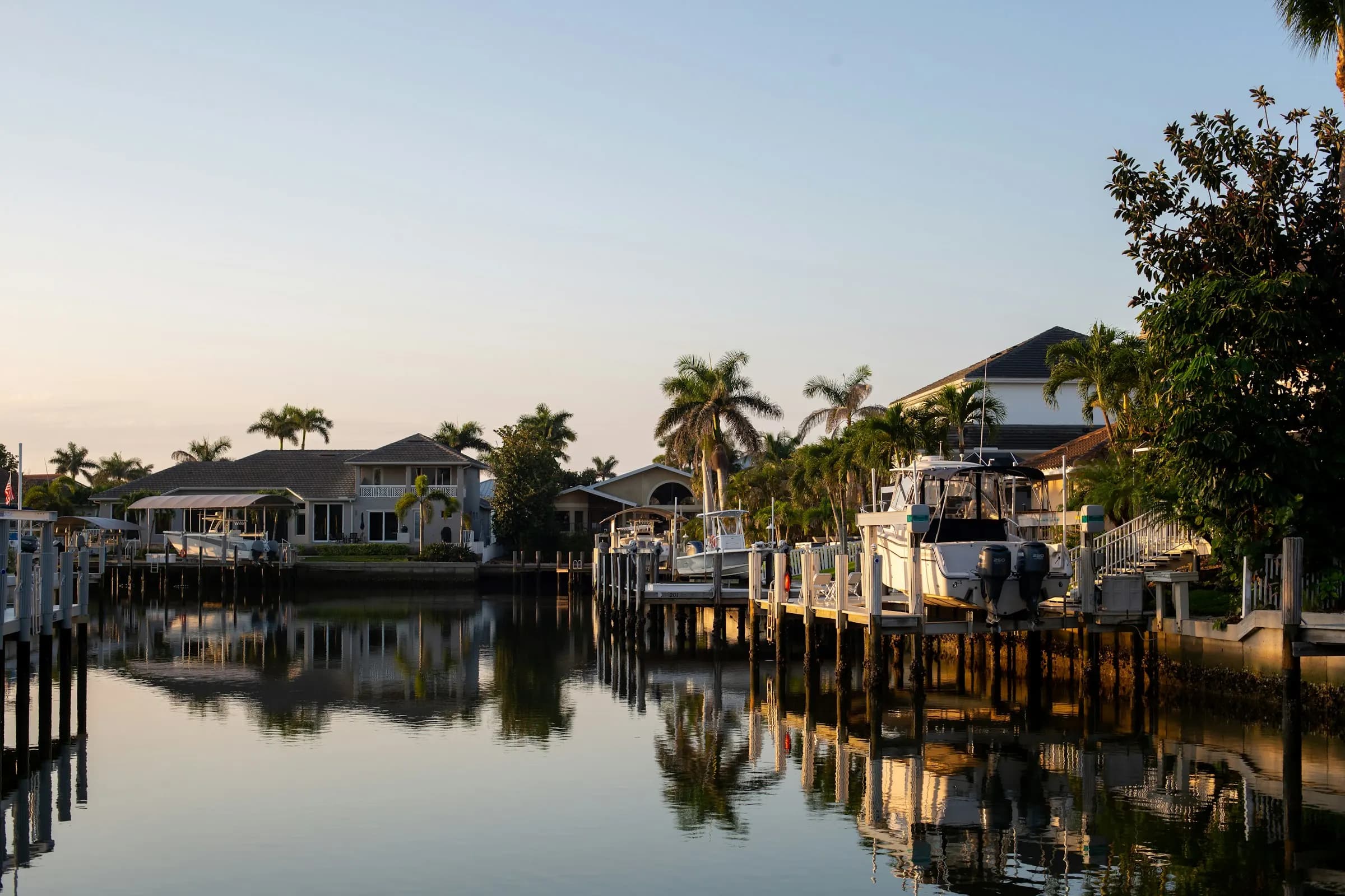 Houses lined along a canal, boats docked at the pier, reflections on the water at sunset